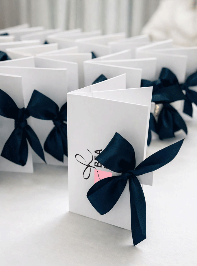 Set bijelih etuija za čokoladice s elegantnom tamnoplavom satenskom mašnom i personaliziranim tiskom.